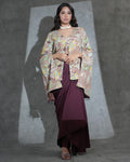 A woman models a traditional outfit featuring a beige and multicolor floral printed shawl draped over a deep maroon dress, set against a textured gray studio backdrop with dramatic lighting.